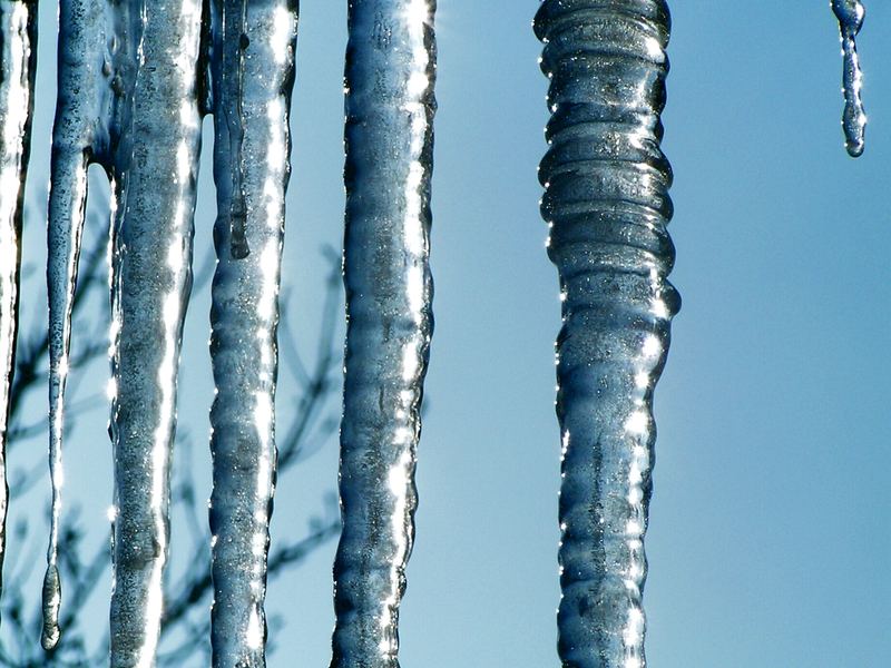 Large icicles hanging from a roofline against a blue winter sky
